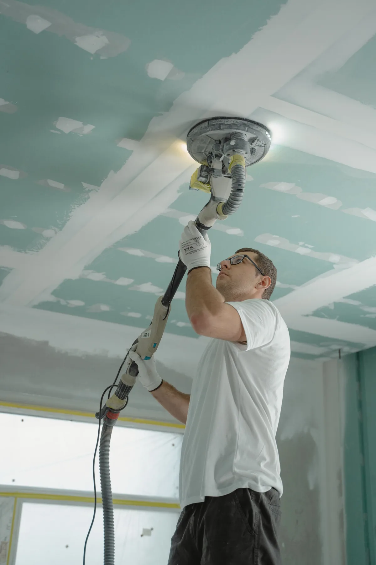 drywall installation cost in Queens NY — contractor sanding a drywall ceiling smooth